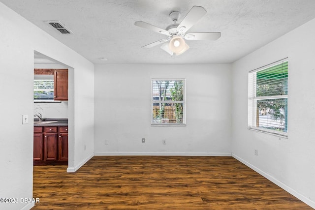 empty room featuring ceiling fan, visible vents, a textured ceiling, and dark wood-style floors