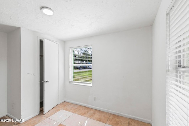 unfurnished bedroom featuring light tile patterned floors, a closet, baseboards, and a textured ceiling