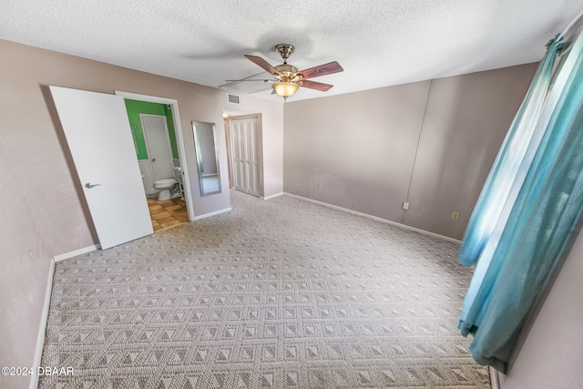 unfurnished bedroom with light carpet, a textured ceiling, connected bathroom, and ceiling fan