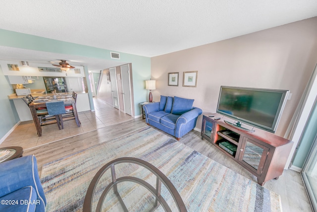 living room with ceiling fan, light hardwood / wood-style floors, and a textured ceiling