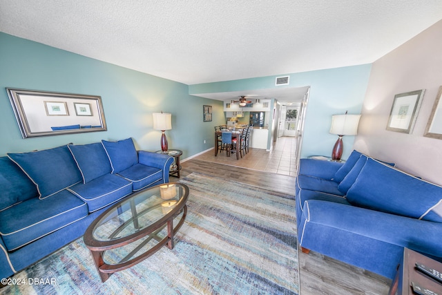 living room with a textured ceiling, light hardwood / wood-style floors, and ceiling fan