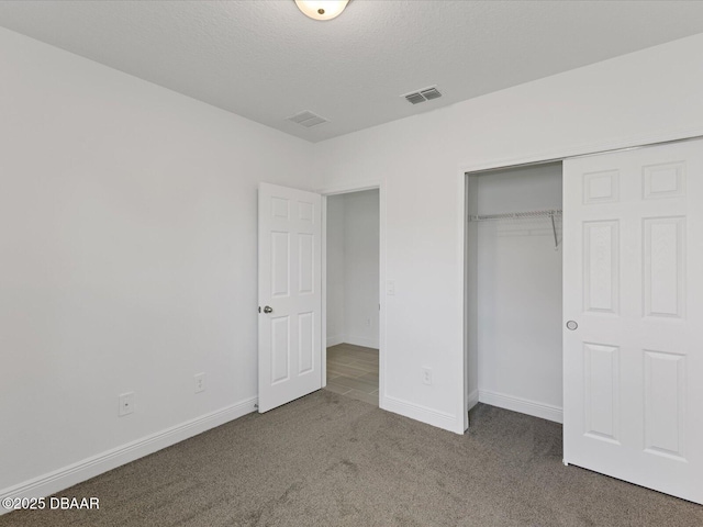 unfurnished bedroom featuring a textured ceiling, a closet, and dark colored carpet