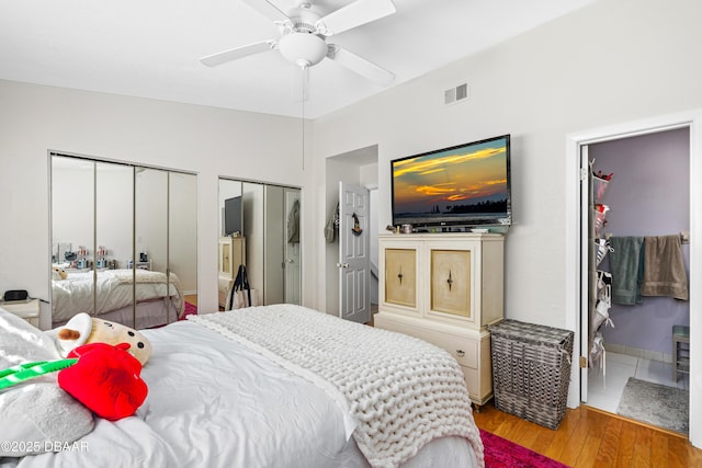 bedroom featuring multiple closets, ceiling fan, ensuite bathroom, and light hardwood / wood-style floors