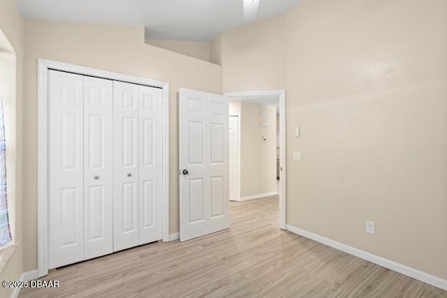 unfurnished bedroom with lofted ceiling, light hardwood / wood-style floors, and a closet