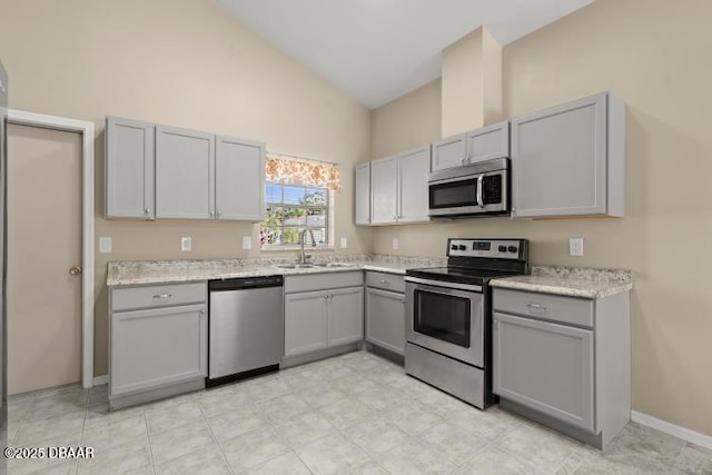 kitchen featuring stainless steel appliances, light stone countertops, gray cabinets, and sink