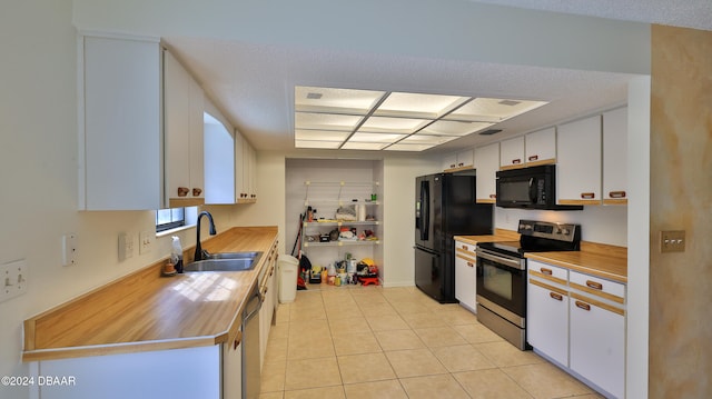 kitchen with white cabinets, sink, light tile patterned floors, black appliances, and a textured ceiling