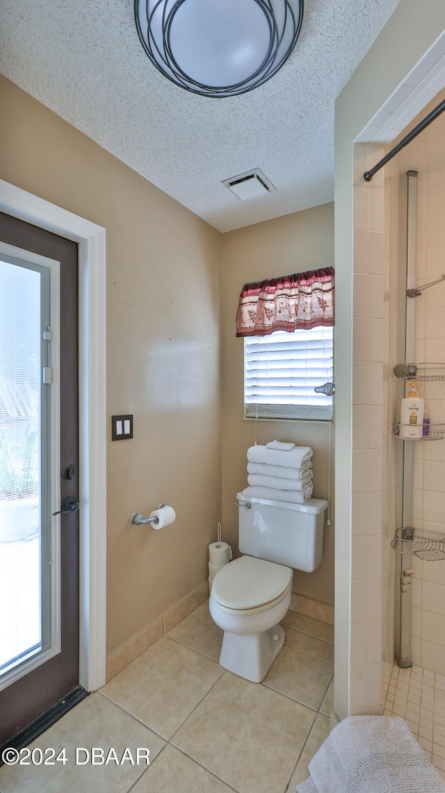 bathroom with tile patterned floors, a tile shower, a textured ceiling, and toilet