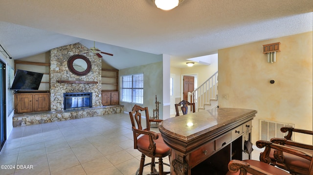 dining space with light tile patterned flooring, lofted ceiling, a textured ceiling, ceiling fan, and a stone fireplace