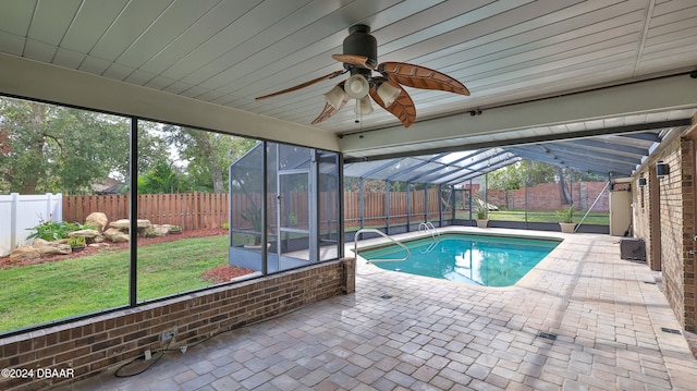 view of pool featuring glass enclosure, ceiling fan, a lawn, and a patio area