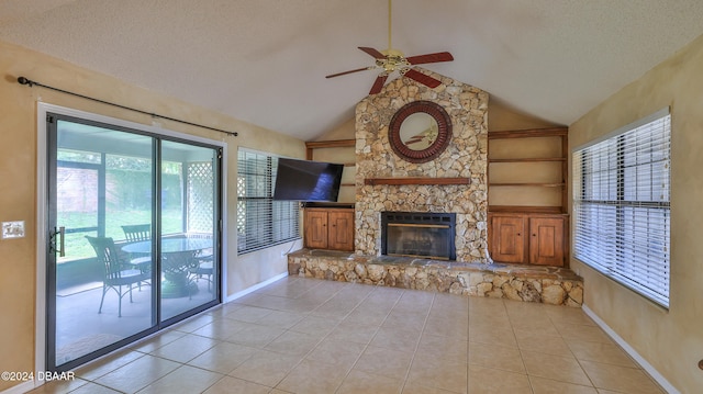 unfurnished living room with high vaulted ceiling, light tile patterned floors, a textured ceiling, ceiling fan, and a stone fireplace