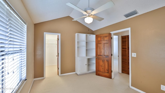 unfurnished bedroom featuring light carpet, a walk in closet, ceiling fan, a closet, and lofted ceiling