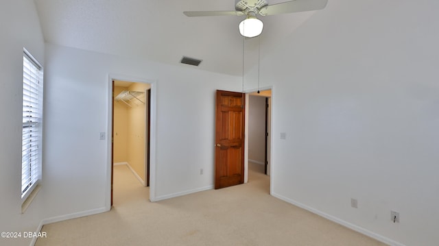 unfurnished bedroom featuring a spacious closet, a closet, ceiling fan, and light carpet