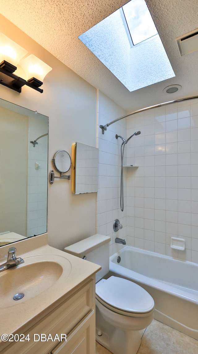 full bathroom with a skylight, tiled shower / bath combo, tile patterned flooring, toilet, and vanity