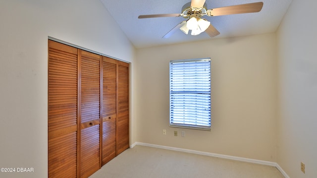 unfurnished bedroom featuring a textured ceiling, light colored carpet, vaulted ceiling, ceiling fan, and a closet