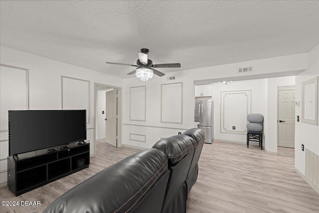 living room with ceiling fan, a textured ceiling, and light wood-type flooring