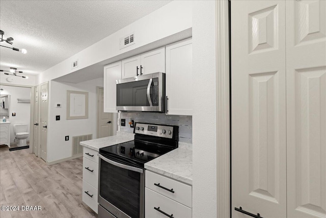 kitchen featuring stainless steel appliances, white cabinetry, light stone counters, a textured ceiling, and light wood-type flooring