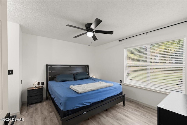 bedroom with ceiling fan, a textured ceiling, and light wood-type flooring