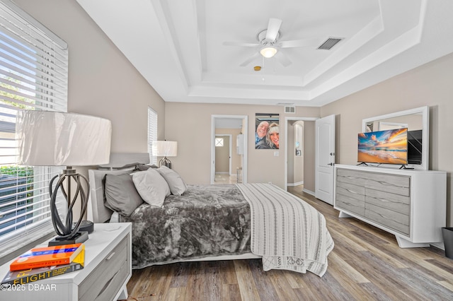 bedroom featuring light wood-type flooring, a raised ceiling, and visible vents