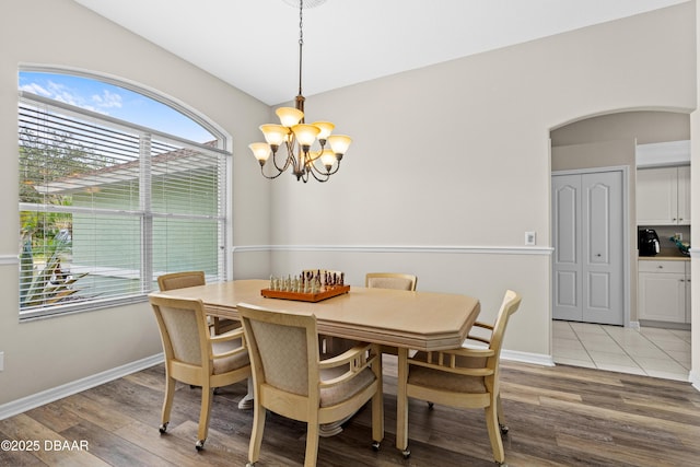 dining space with arched walkways, light wood-style flooring, baseboards, and an inviting chandelier