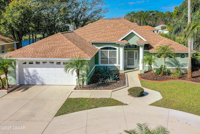 view of front of house featuring driveway, stucco siding, roof with shingles, an attached garage, and a front yard