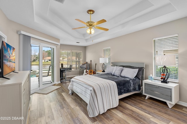 bedroom with hardwood / wood-style floors, access to outside, ceiling fan, and a tray ceiling