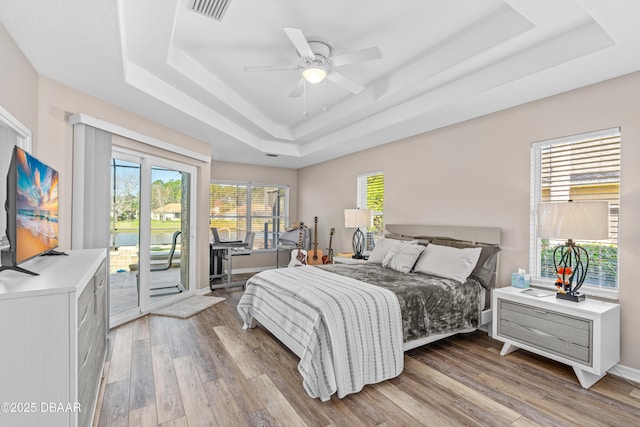 bedroom featuring access to outside, light wood finished floors, a raised ceiling, and visible vents