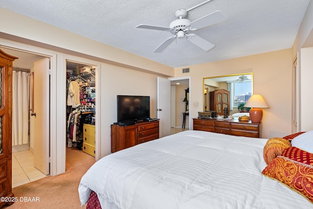 bedroom featuring light carpet, a textured ceiling, a walk in closet, and ceiling fan