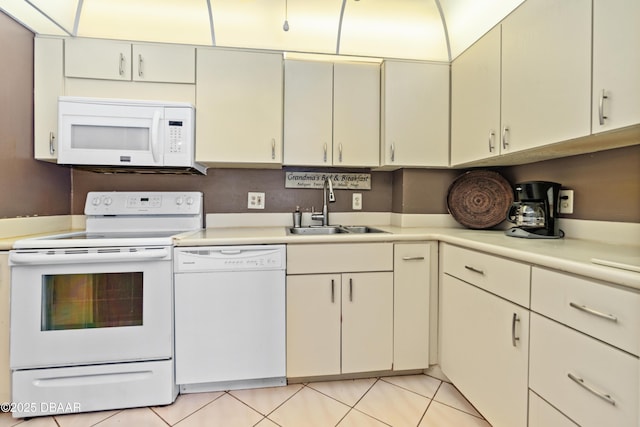 kitchen with light tile patterned flooring, cream cabinets, white appliances, and sink