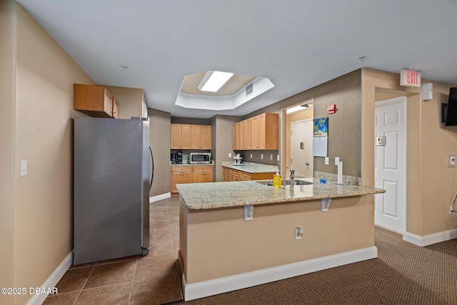 3737 S Atlantic Ave Unit 702, Daytona Beach, FL 32118 - kitchen featuring appliances with stainless steel finishes, a peninsula, a kitchen breakfast bar, light stone counters, and light brown cabinetry