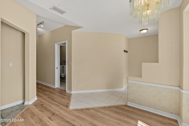 spare room featuring an inviting chandelier, light wood-style floors, visible vents, and baseboards