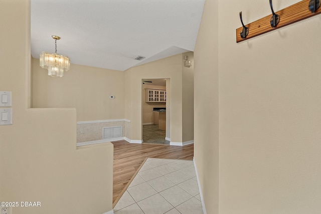 hallway with vaulted ceiling, light tile patterned flooring, visible vents, and a chandelier