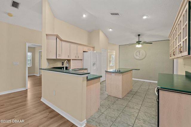 kitchen with dark countertops, a center island, lofted ceiling, white refrigerator with ice dispenser, and a ceiling fan