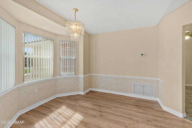 empty room with visible vents, baseboards, an inviting chandelier, and wood finished floors