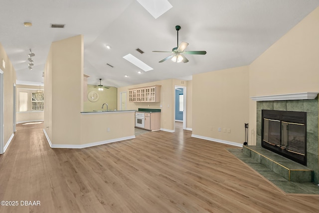 unfurnished living room featuring visible vents, vaulted ceiling with skylight, a tile fireplace, light wood-style floors, and a ceiling fan