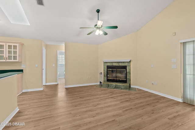 unfurnished living room featuring visible vents, lofted ceiling with skylight, a tiled fireplace, light wood-type flooring, and a ceiling fan