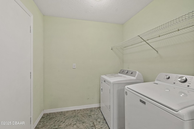 clothes washing area with a textured ceiling, laundry area, baseboards, and washer and clothes dryer