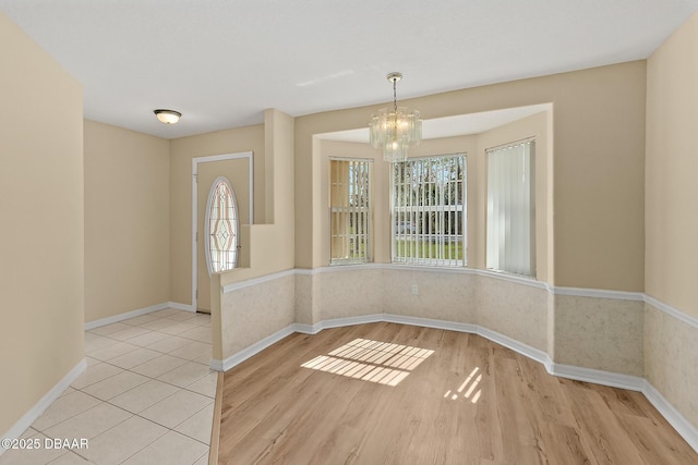 unfurnished dining area featuring light wood finished floors, plenty of natural light, baseboards, and an inviting chandelier