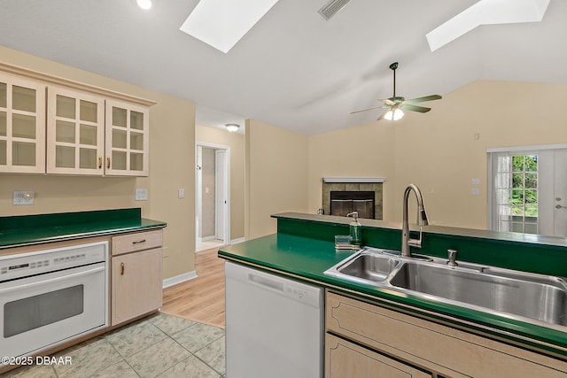 kitchen featuring visible vents, a sink, white appliances, vaulted ceiling with skylight, and a fireplace