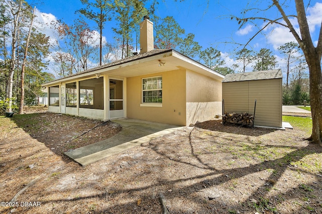 rear view of property featuring stucco siding, a storage shed, an outdoor structure, a sunroom, and a chimney