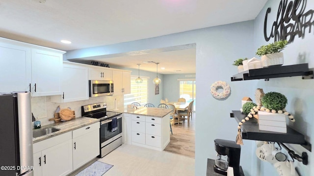 8 Tarpon Ave, Ormond Beach, FL 32176 - kitchen with appliances with stainless steel finishes, a peninsula, white cabinetry, decorative backsplash, and decorative light fixtures