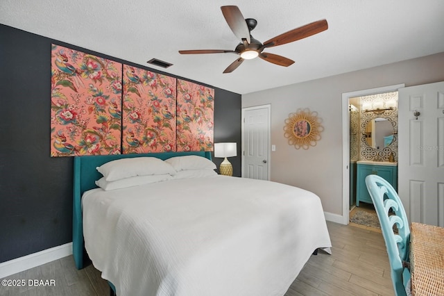 bedroom featuring wood finished floors, baseboards, a ceiling fan, a textured ceiling, and ensuite bathroom