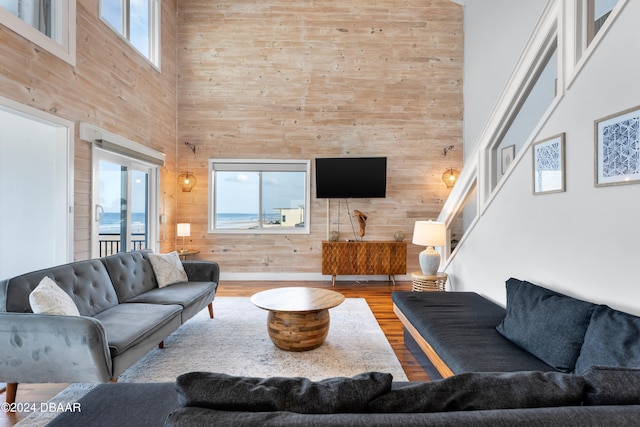 living room featuring a towering ceiling, plenty of natural light, wood walls, and hardwood / wood-style flooring