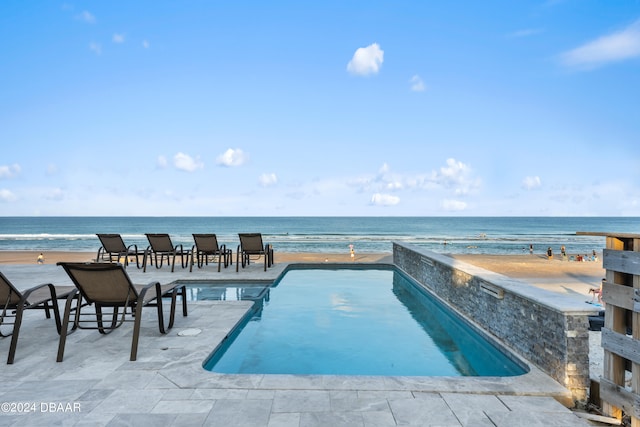 view of pool with a patio area, a water view, and a view of the beach