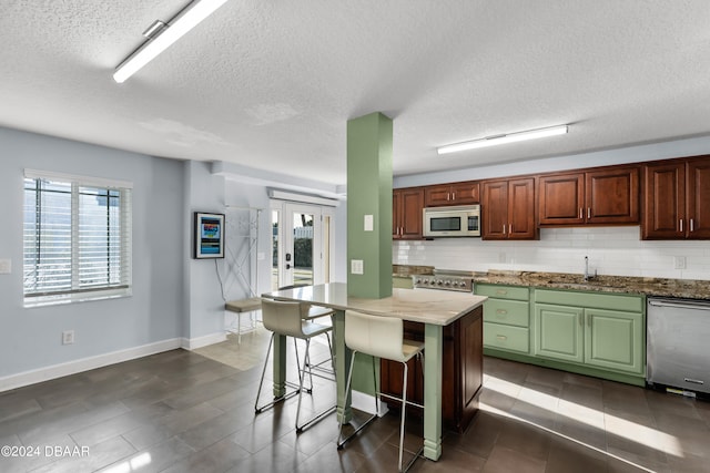 kitchen featuring stainless steel appliances, a textured ceiling, tasteful backsplash, a breakfast bar area, and sink