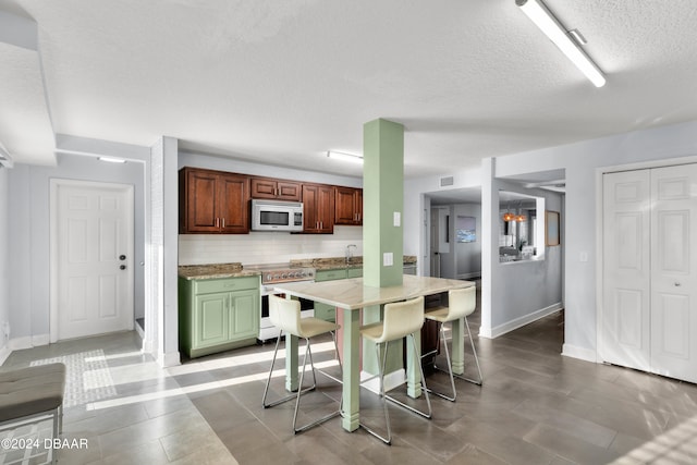 kitchen with tile patterned floors, a textured ceiling, decorative backsplash, a breakfast bar, and white appliances