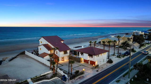 aerial view at dusk featuring a view of the beach and a water view