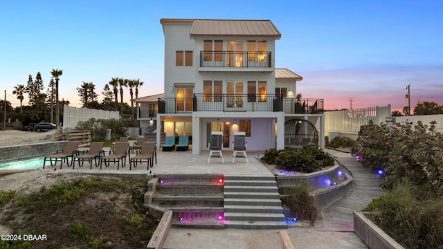 back house at dusk with a balcony, a fenced in pool, pool water feature, and a patio area