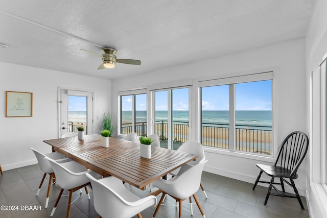 dining space featuring a water view, ceiling fan, a textured ceiling, tile patterned floors, and a beach view