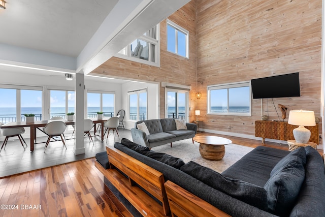 living room featuring hardwood / wood-style flooring, beamed ceiling, a water view, a towering ceiling, and wooden walls