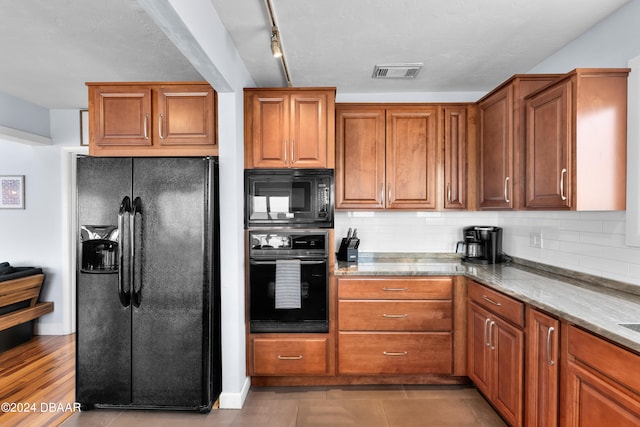 kitchen with light wood-type flooring, decorative backsplash, black appliances, and light stone counters